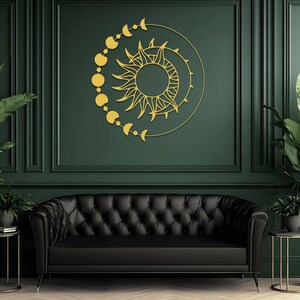 May include: A gold-colored sun and moon wall art decorates a dark green wall above a black tufted sofa. The sun has detailed rays and is surrounded by a crescent moon and phases of the moon. Potted plants flank the sofa.