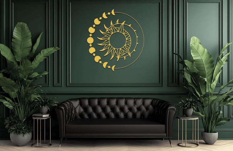 May include: A gold-colored sun and moon wall art decorates a dark green wall above a black tufted sofa. The sun has detailed rays and is surrounded by a crescent moon and phases of the moon. Potted plants flank the sofa.