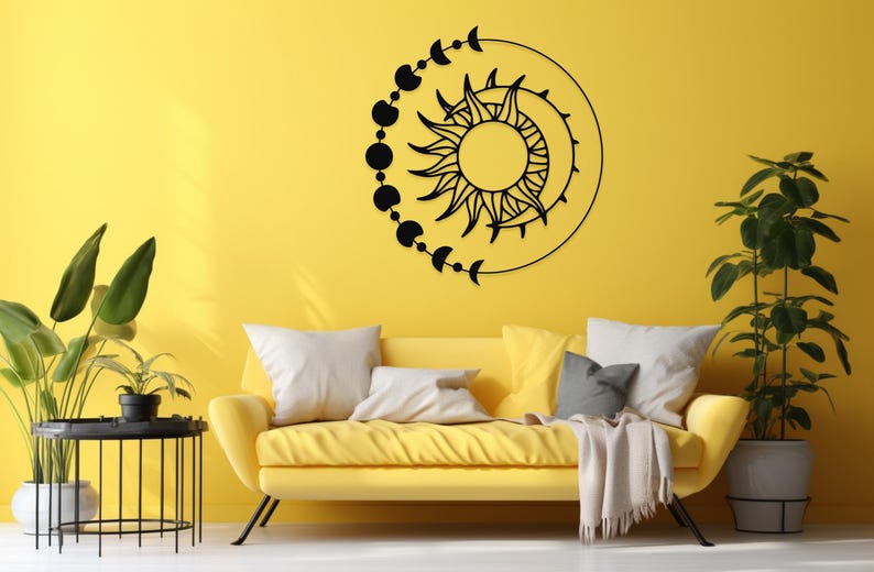 May include: Black metal wall art featuring a sun and moon design with phases of the moon. The artwork is circular and mounted on a yellow wall above a yellow sofa with white and gray pillows. Decorative home decor.