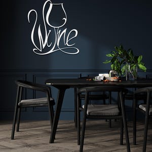 May include: White metal wall art spelling "Wine" in a cursive font, with a wine glass design. The art is mounted on a dark blue wall above a black dining table and chairs. The room has a modern, minimalist aesthetic.