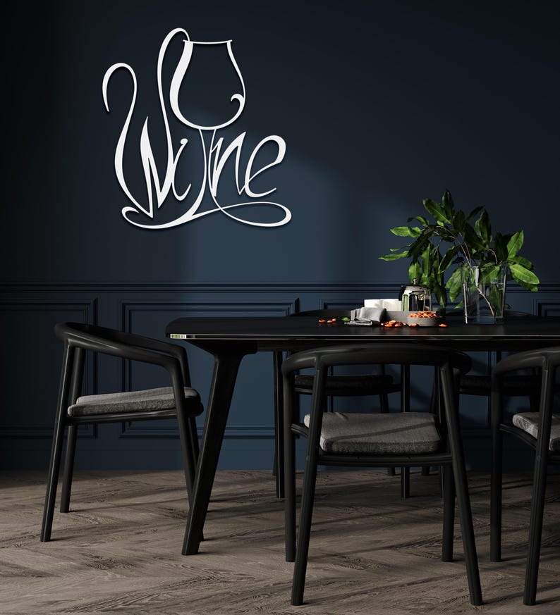 May include: White metal wall art spelling "Wine" in a cursive font, with a wine glass design. The art is mounted on a dark blue wall above a black dining table and chairs. The room has a modern, minimalist aesthetic.