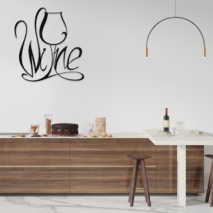 May include: Black metal wall art featuring the word "Wine" in a stylized script, with a wine glass incorporated into the design. The art is mounted on a white wall above a kitchen counter with a cake and wine bottle.