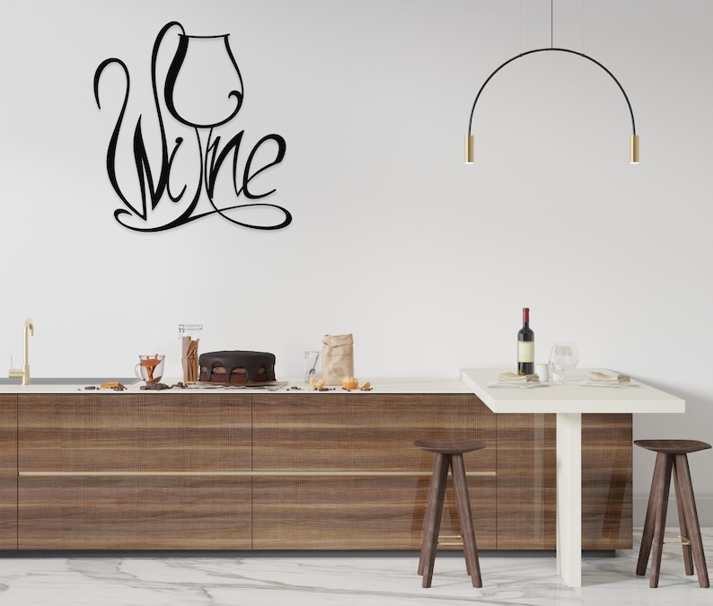 May include: Black metal wall art featuring the word "Wine" in a stylized script, with a wine glass incorporated into the design. The art is mounted on a white wall above a kitchen counter with a cake and wine bottle.