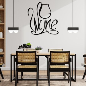 May include: A dining room scene featuring a wooden table and four chairs with woven seats. A black metal sign on the wall spells "Wine" in a stylized font. Two black pendant lights hang above the table.