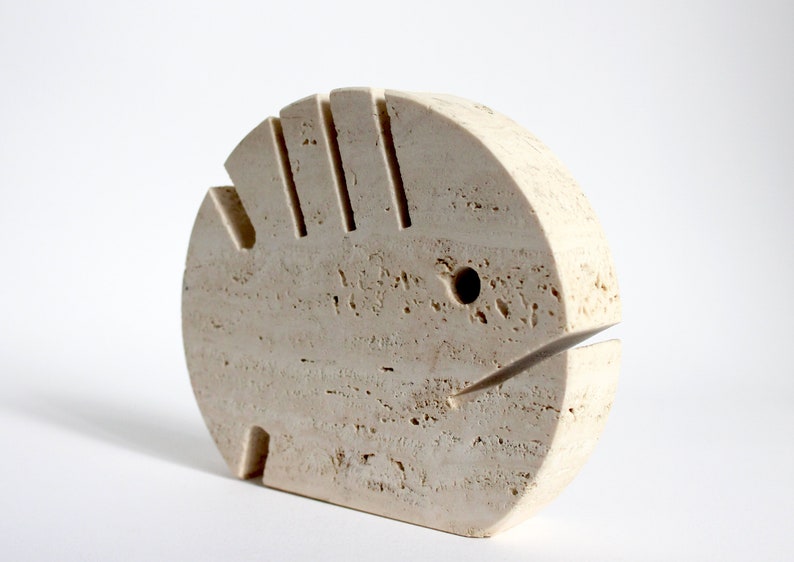 K&ouml;nnte beinhalten: Eine beige Steinskulptur eines Fisches mit einem geschnitzten Mund und Auge. Die Skulptur ist aus Travertin und hat eine raue, strukturierte Oberfl&auml;che.