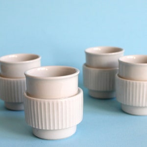 Könnte beinhalten: Vier weiße Keramikbecher mit geripptem Design. Die Becher sind übereinander gestapelt.