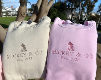 May include: Two sweatshirts, one cream and one pink, with a Mickey Mouse silhouette and the text "Mickey & Co. Est. 1928" embroidered on the front.