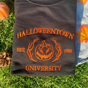 May include: Black sweatshirt with orange embroidered text that reads "HALLOWEENTOWN EST. 1998 UNIVERSITY" and a pumpkin with a scary face.