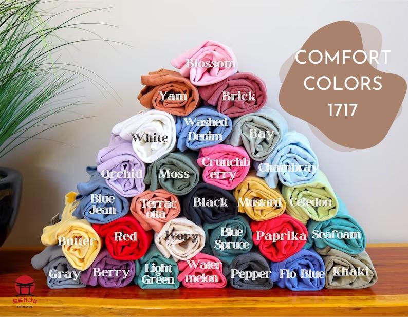 Puede incluir: Una pila de muestras de tela enrolladas en varios colores, incluyendo azul, verde, rojo y amarillo. Las muestras de tela est&aacute;n etiquetadas con nombres como "Berry", "Seafoam", "Watermelon" y "Paprika". El texto "COMFORT COLORS 1717" se muestra encima de las muestras de tela.