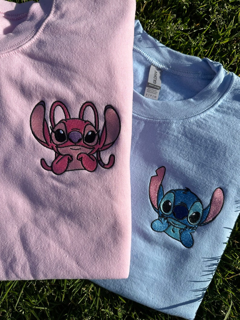 Puede incluir: Dos camisetas con personajes de Stitch bordados. La camiseta rosa tiene un Stitch rosa con un fondo azul claro. La camiseta azul tiene un Stitch azul con un fondo blanco.