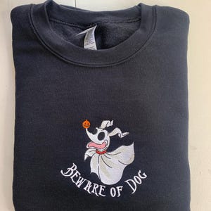 Puede incluir: Sudadera negra con una imagen bordada en blanco de un perro fantasma sosteniendo una calabaza con el texto "Beware of Dog" debajo.