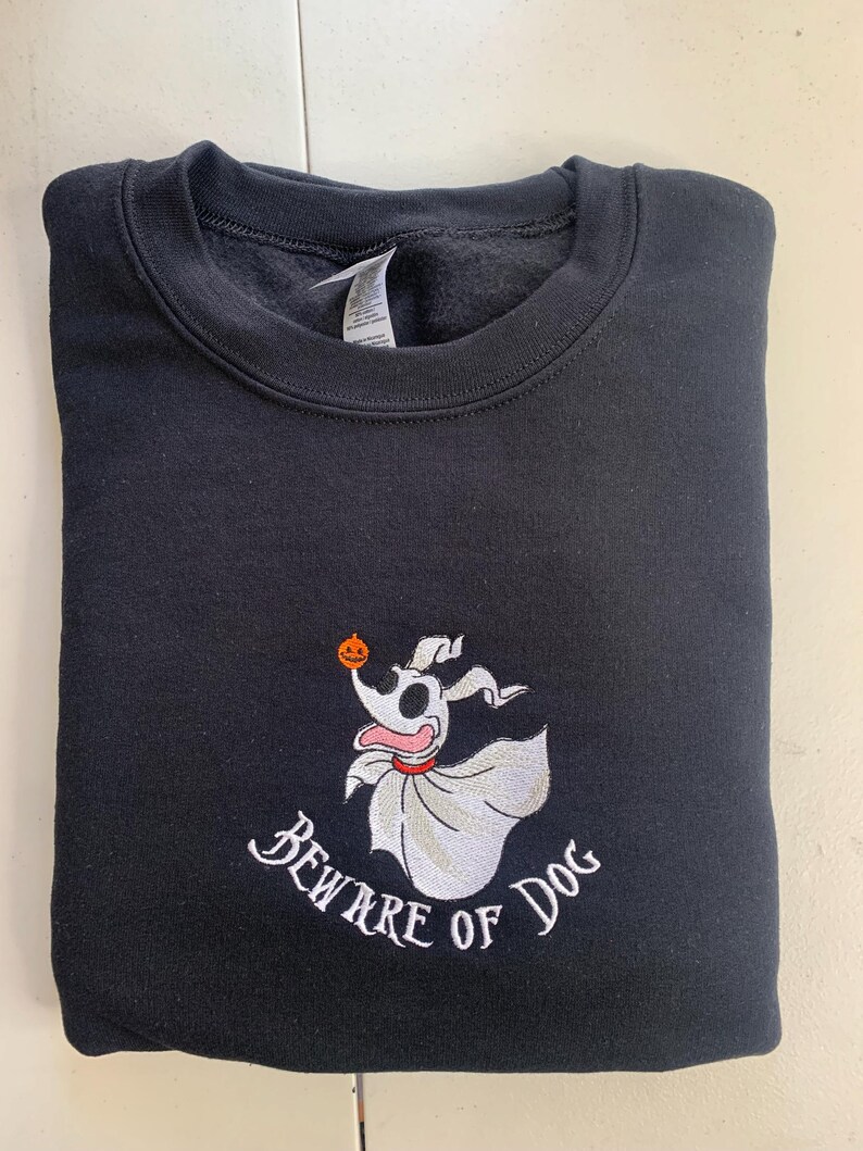 Puede incluir: Sudadera negra con una imagen bordada en blanco de un perro fantasma sosteniendo una calabaza con el texto "Beware of Dog" debajo.