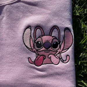 Puede incluir: Camiseta rosa con una imagen bordada de Stitch, un personaje alien&iacute;gena rosa de la pel&iacute;cula de Disney Lilo & Stitch. Stitch se muestra con la lengua fuera y los brazos cruzados.