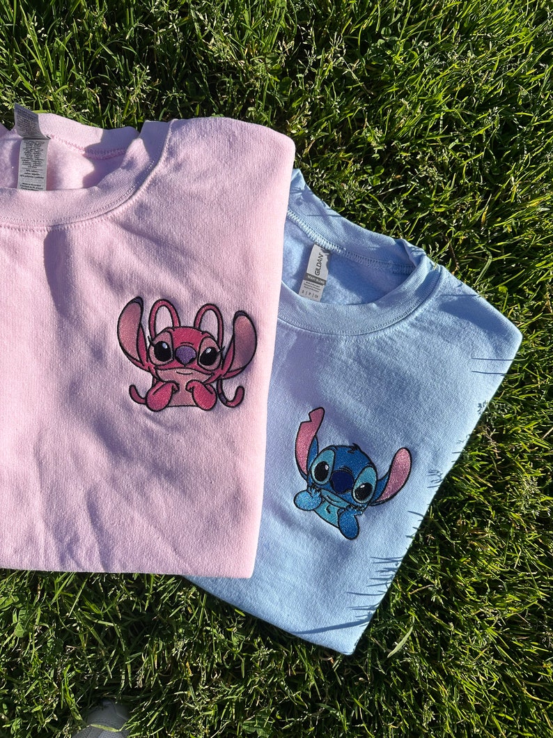 Puede incluir: Dos camisetas con personajes de Stitch bordados. La camiseta de la izquierda es rosa con un personaje de Stitch rosa. La camiseta de la derecha es azul claro con un personaje de Stitch azul.
