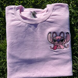 Puede incluir: Sudadera rosa con una peque&ntilde;a imagen bordada de Stitch de Lilo & Stitch. Stitch lleva gafas y saca la lengua.