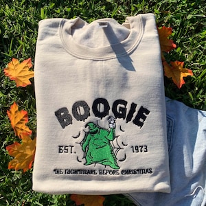 May include: A beige sweatshirt with a green and black embroidered design of a character from "The Nightmare Before Christmas" with the text "Boogie Est. 1973 The Nightmare Before Christmas".