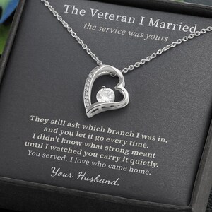 Puede incluir: Un collar con colgante en forma de corazón plateado y una piedra redonda transparente en el centro, presentado en una caja negra con el texto: The Veteran I Married, the service was yours. They still ask which branch I was in.