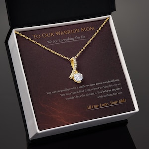 Op de afbeelding: Een goudkleurige hangerketting met een heldere, ronde edelsteen. De ketting wordt gepresenteerd in een geschenkdoos met de tekst "TO OUR WARRIOR MOM" en een liefdevolle boodschap van kinderen.