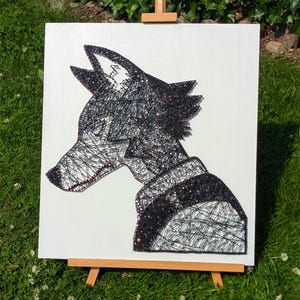 May include: A black and white string art piece depicting a wolf's profile. The artwork is mounted on a white canvas and displayed on a small wooden easel. The wolf's fur is detailed with black glitter.