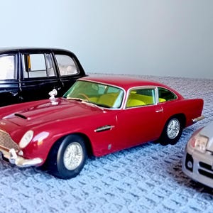 May include: A collection of four toy cars, including a black taxi, a red sports car, a silver car, and a red and black car. The cars are arranged on a grey surface.