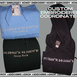 May include: Two hooded sweatshirts with custom embroidered coordinates. The blue sweatshirt has the coordinates 48.58952&deg;N 93.16879&deg;W and the text "Steep Rock". The black sweatshirt has the coordinates 27.7599&deg; 54.0066&deg;E. Both sweatshirts have the text "@howdyembroidery" embroidered on them.