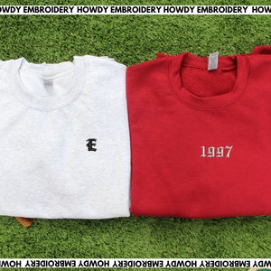 May include: Two sweatshirts, one light gray with a black embroidered letter "E" and one red with a silver embroidered "1997".