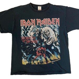 May include: Black t-shirt featuring the band name "Iron Maiden" in red letters above a graphic from "The Number of the Beast" album. The graphic includes a skeletal figure and a red demon-like character.