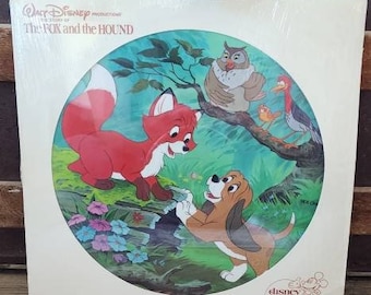 May include: A vintage Disney picture disc record featuring the characters from the animated film "The Fox and the Hound". The disc shows a red fox and a brown and white hound dog standing on a green forest background with a bluebird, an owl, and a red bird.