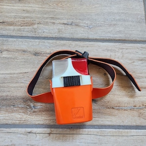 May include: An orange and white dog training device with a black and orange strap. The device has a red and white light on top and the word "wonder" printed on the side.