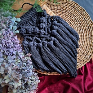 May include: A black macrame wall hanging with a geometric pattern and long fringe tassels.