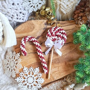 Könnte beinhalten: Ein roter und weißer Zuckerstangen und ein roter und weißer Wirbel-Lolli mit einer weißen Schleife auf einer Holzoberfläche.
