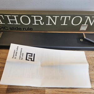 May include: A white ceramic mug with a black handle and the text "But First, Coffee" in a bold, black font. The mug is set against a blurred background, highlighting its clean design.