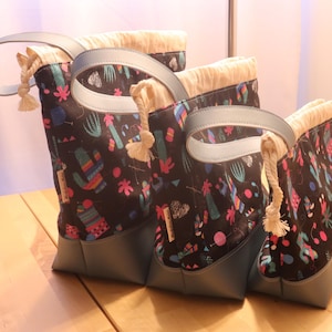 May include: Set of three tote bags with a black cactus print. The bags have light blue handles and bases, and a cream-colored drawstring closure. The bags are different sizes, with the largest bag standing approximately 12 inches tall.