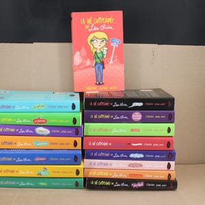 May include: A collection of fifteen books titled La vie compliquée de Léa Olivier by Catherine Girard-Audet, featuring one upright book with a cartoon illustration and fourteen stacked books showing colorful spines with various text and graphic details.