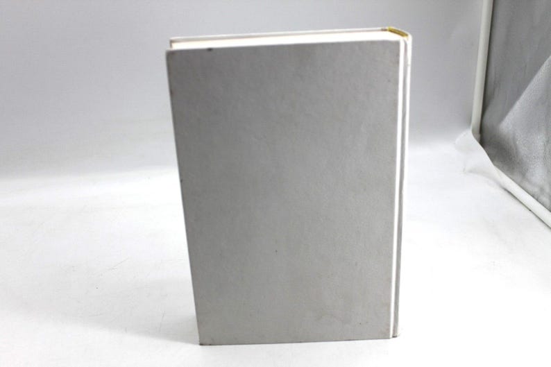 May include: A hardcover book with a light gray cover and white pages. The spine is white, and the top corner has a gold accent. The book is standing upright on a white surface.