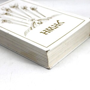 May include: A white book with gold lettering and illustrations. The cover features an ornate design and the letters "HMHK". The book's pages are visible, and the spine is a darker color. The book is on a white surface.