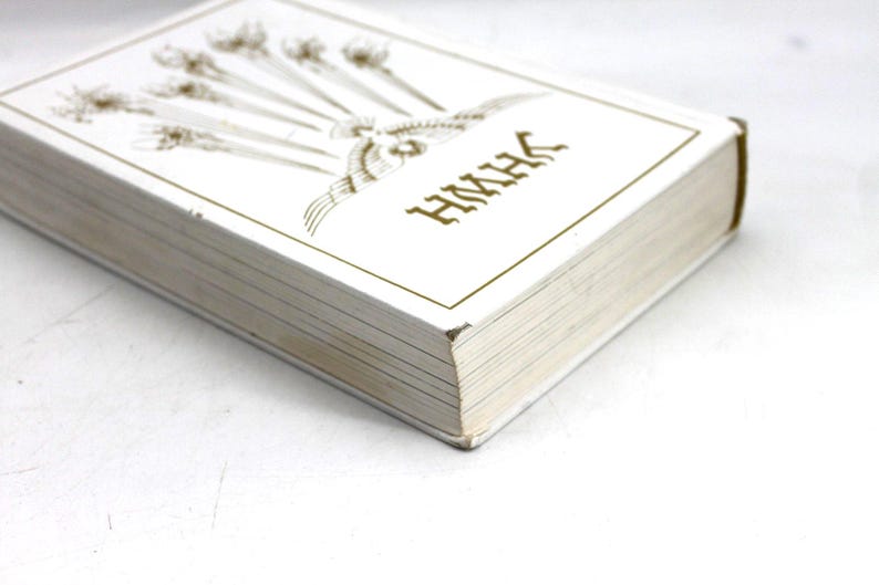 May include: A white book with gold lettering and illustrations. The cover features an ornate design and the letters "HMHK". The book's pages are visible, and the spine is a darker color. The book is on a white surface.