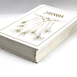 May include: A hardcover book with a white cover and gold lettering and illustrations. The title "YHWH" is at the top. The book's pages are visible, and the edges are slightly worn.