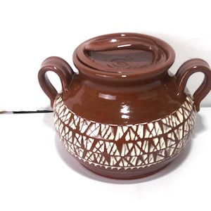 Peut inclure: Un pot en céramique brun avec un motif géométrique blanc et un couvercle. Le pot a deux anses et est de style traditionnel.