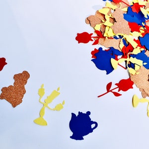May include: A collection of confetti featuring various characters from the Disney movie Beauty and the Beast. The confetti is made of paper and features a gold glitter finish. The characters include a rose, a teapot, a candlestick, and a prince.