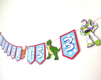 May include: A birthday banner featuring the name "ARTHUR" and the number "3" on blue and red pennants. The banner includes cartoon character cutouts and is strung on a red and white twine. A Buzz Lightyear cutout is also included.