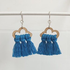 May include: A pair of handmade earrings featuring a cloud-shaped wooden cutout with three blue tassels. The earrings have silver-colored hooks. The tassels are a vibrant shade of blue.