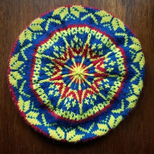 May include: A knitted beret with a colorful geometric pattern in shades of yellow, blue, and red. The pattern is a repeating design of stars and diamonds.