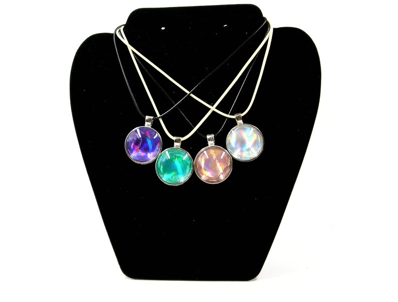 May include: Four necklaces with iridescent glass pendants on a black display stand. The pendants are in shades of purple, green, pink, and white.