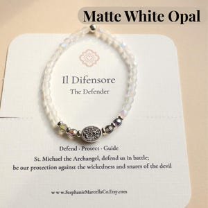 May include: A matte white opal bracelet with a silver centerpiece and iridescent beads. The bracelet is displayed on a card with the text "Il Difensore, The Defender" and "Defend, Protect, Guide". The card also includes the website www.StephanieMarcellaCo.Etsy.com.