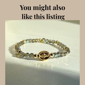 May include: A beaded stretch bracelet with a gold-colored centerpiece and beads. The bracelet features a gold-colored oval centerpiece with an engraved design. The beads are a mix of clear and iridescent, with gold-colored accent beads.