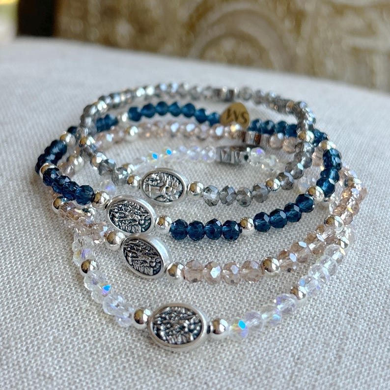 May include: A set of five bracelets with silver oval charms and crystal beads in shades of blue, gray, and clear.