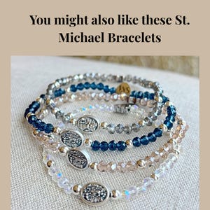 May include: Several beaded bracelets in shades of blue, clear, and pink. Each bracelet features small, round beads and a silver oval charm. The text "You might also like these St. Michael Bracelets" is at the top.