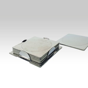 Può includere: Un set di sottobicchieri quadrati in metallo con un design circolare al centro. I sottobicchieri sono impilati in un supporto di metallo, con un sottobicchiere posizionato separatamente. I sottobicchieri hanno una finitura in metallo spazzolato.