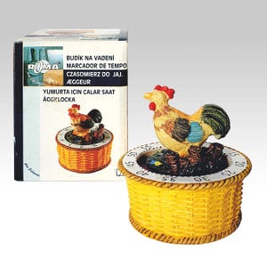 May include: A kitchen timer in the shape of a yellow woven basket, topped with a colourful rooster figurine. The timer has a white dial with numbers. The box includes text in multiple languages, including 'Egg Timer'.